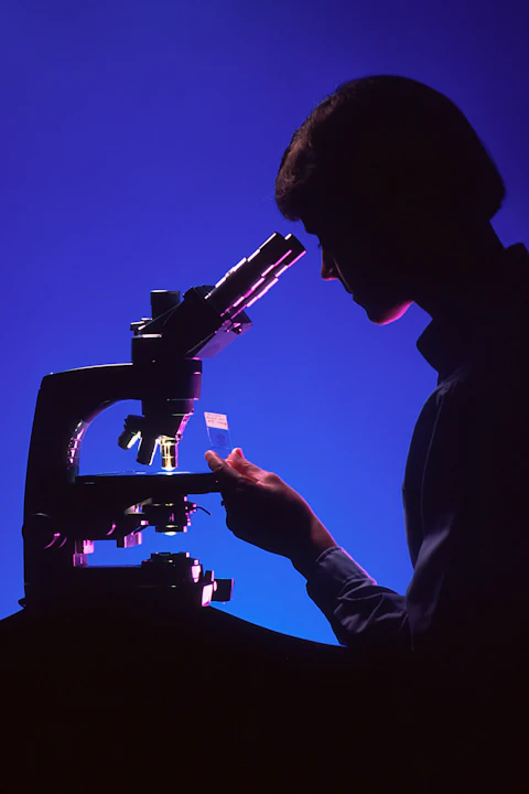 A pathologist looking through a microscope in blue and magenta light